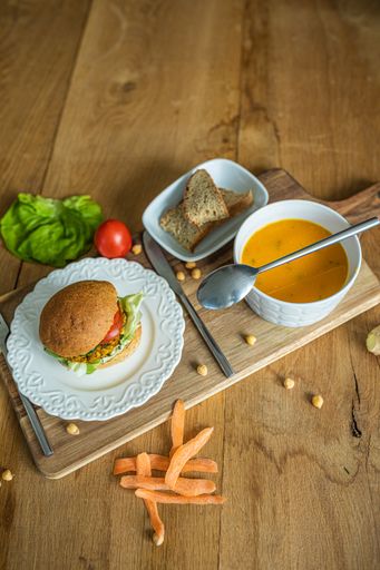 A delicious veggie burger and a bowl of pumpkin soup on a wooden board in the kitchen