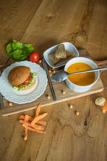A delicious veggie burger and a bowl of pumpkin soup on a wooden board in the kitchen