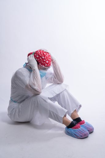 A vertical shot of an upset nurse in medical uniform sitting on the floor and holding her head