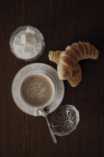 A top view of homemade cheese rolls with a cup of cappuccino and sugar on a table