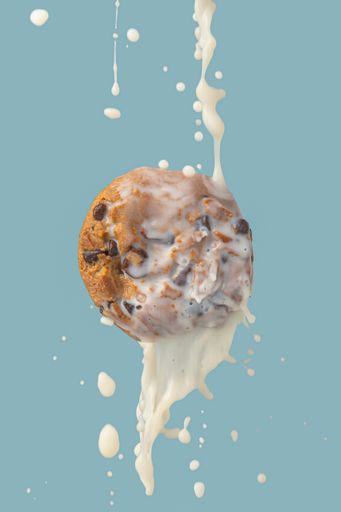 A vertical shot of the milk splashing on the cookie from above on a blue background