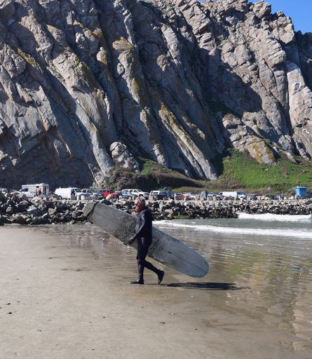 A photo of a Mature Man walking on the beach with his Surfboard