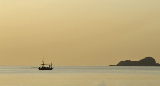 A silhouette of a fishermn collecting fishing gear on a small fishing boat