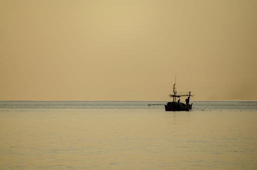 The silhouette of fishermen collecting fishing gear on a small fishing boat