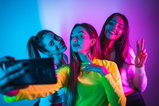 A portrait of young beautiful Caucasian women taking a selfie in a nightclub with blue and pink neon lights looking at a camera