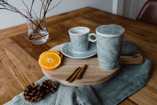 A cup of tea served with cinnamon sticks and slices of ripe orange on a wooden board