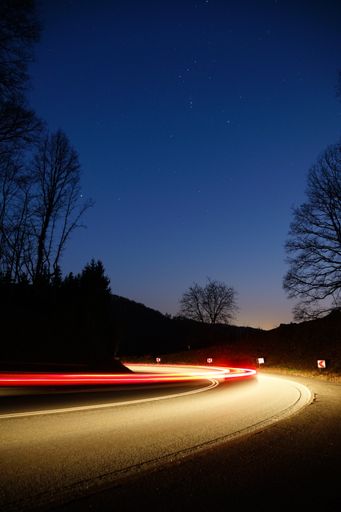 A long exposure of front and rear light trails of a moving car on a winding road during blue hour