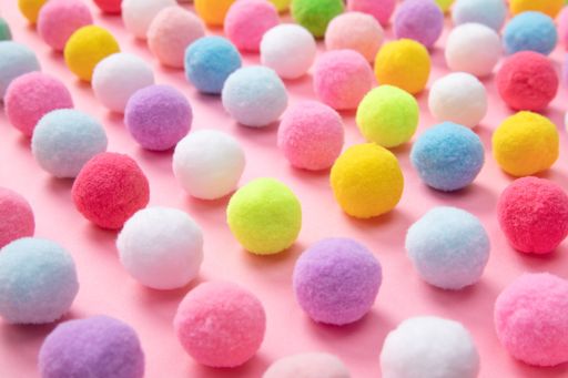 The colorful soft pom pom balls on pink background