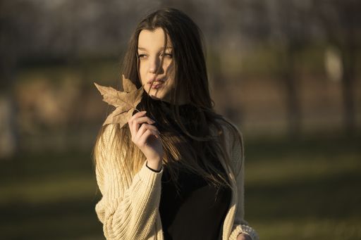 A closeup shot of a Caucasian beautiful woman keeping an autumn leaf on her hand