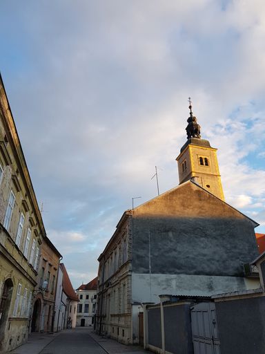 A low angle shot of a church tower illuminated with the sun under a cloudy sky in Varazdin, Croatia
