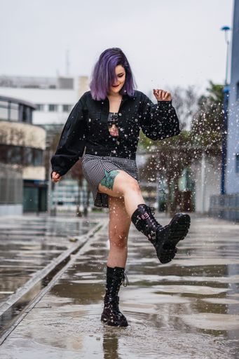 A vertical shot of a stylish European female splashing water from a puddle after the rain