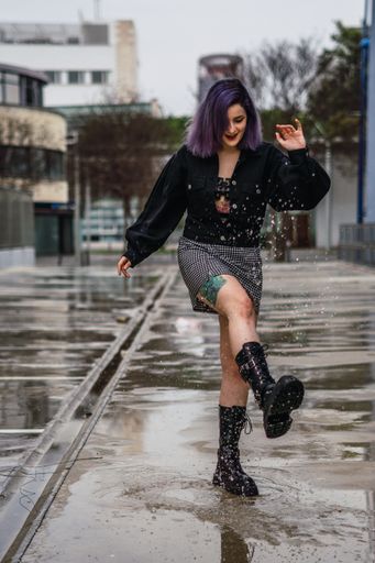 A vertical shot of a young European female with purple hair splashing water from a puddle after the rain