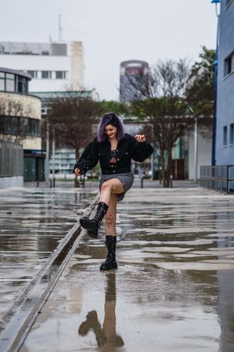 A vertical shot of a stylish European female splashing water from a puddle after the rain