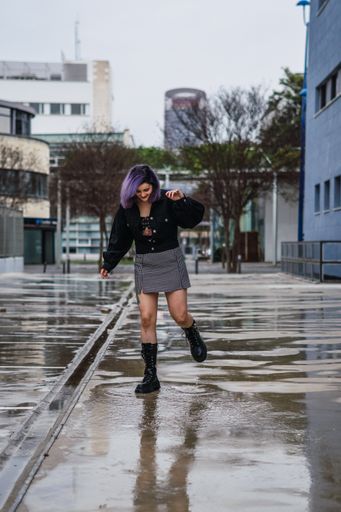 A vertical shot of a stylish European female splashing water from a puddle after the rain