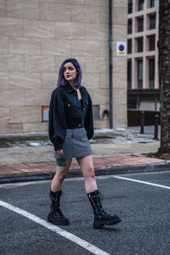 A vertical shot of a stylish European female with purple hair and tattoos walking outdoors
