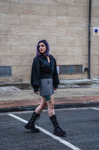 A vertical shot of a stylish European female with purple hair and tattoos walking outdoors