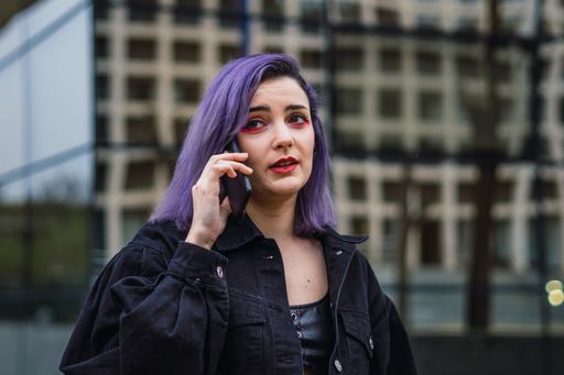 A closeup shot of a Caucasian sexy woman with purple hairs chatting on the phone in the building background