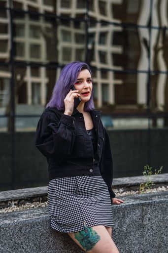 A vertical shot of a young European female with purple hair talking on h phone outdoors