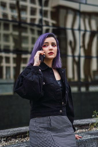 A vertical shot of a Caucasian sexy woman with purple hairs leaning on the wall and chatting on the phone
