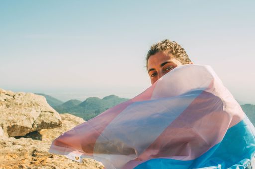 A young Spanish man with the trans flag on his shoulders on a peak of a mountain