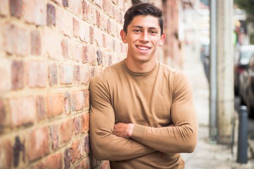 A shallow focus of a smiling young Colombian guy leaning on a wall