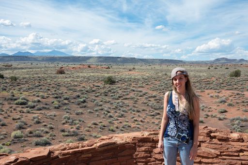 Portrait of a smiling long-haired blonde young girl with backwards cap in the arid desert in summer, she carries her backpack and photo camera