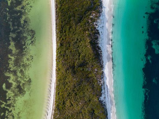 Idyllic panoramic shot of a seascape featuring turquoise waves crashing against the jagged coastline surrounded by lush green foliage