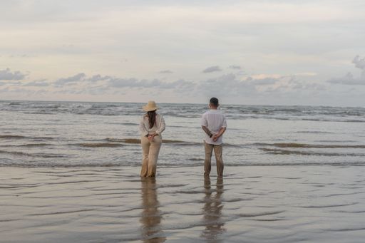 A young couple standing on the sandy shore enjoying the seascape.
