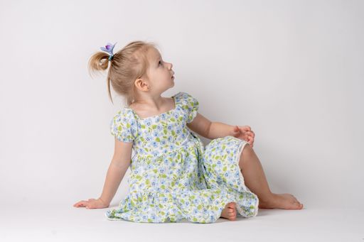 An adorable young girl wearing a floral dress posing on a white background