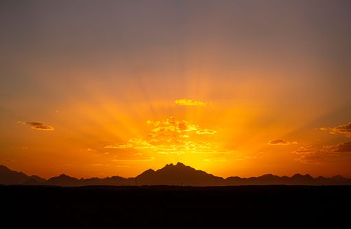 A picturesque landscape of a mountain range, illuminated by the brilliant golden hues of the setting sun