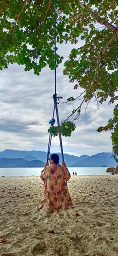 A vertical shot of a lady swinging on the sandy beach in summer