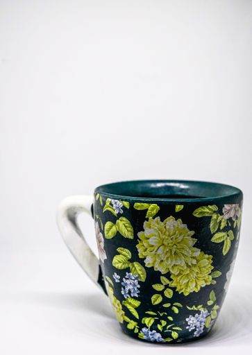A green ceramic cup with floral patterns is displayed on a white countertop, creating a modern and stylish contrast