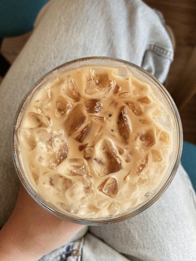 A top view of a female hand holding a big glass cup of iced coffee