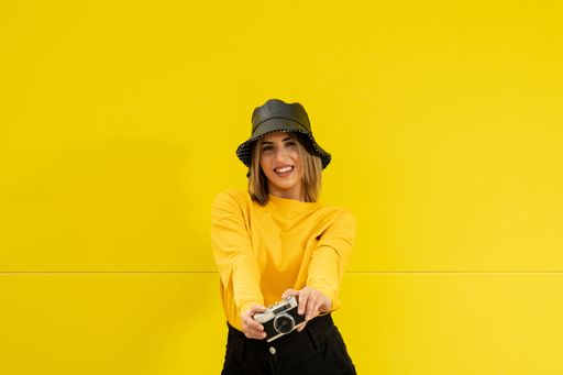A closeup shot of a young Caucasian smiling lady in yellow holding a photo camera