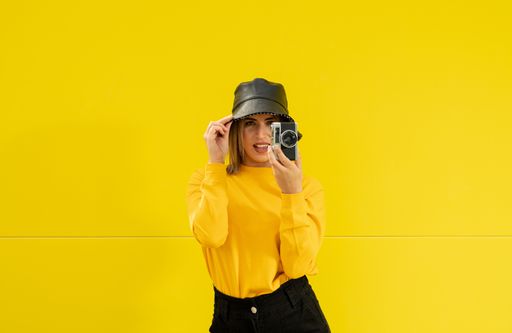 A closeup shot of a young Caucasian lady in yellow with a camera posing for a photo