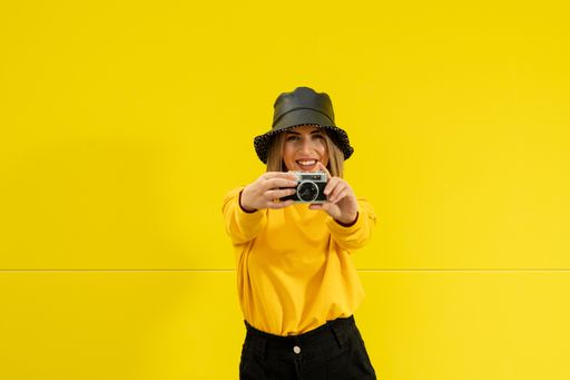 A closeup shot of a young Caucasian smiling lady in yellow holding a photo camera