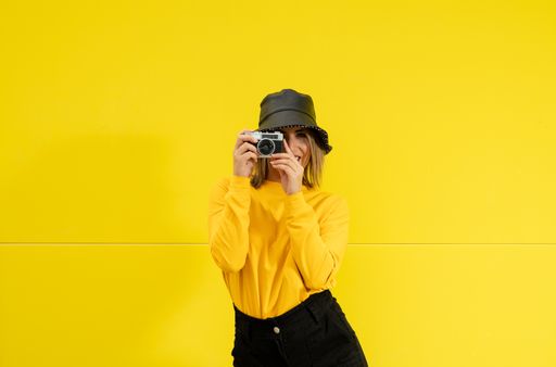 A closeup shot of a young Caucasian smiling lady in yellow taking a photo