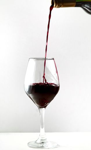 A bottle of red wine being poured into a glass, ready for consumption