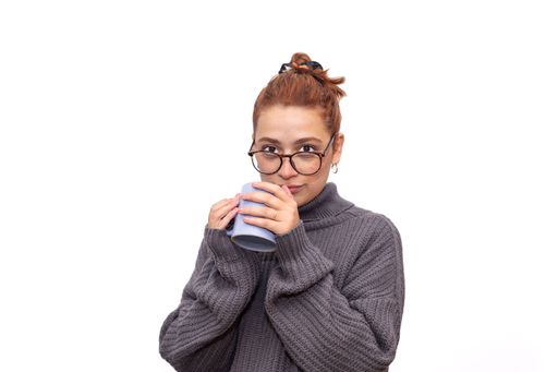 young redhead woman with glasses drinking from a cup staring at the camera