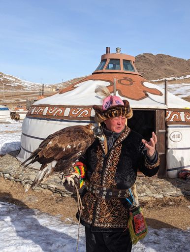 An older male in a traditional fur outfit holding a trained vulture in Ulaanbaatar, Mongolia