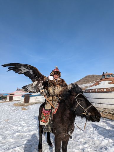 An older male in a traditional fur outfit holding a trained vulture on a horse in Ulaanbaatar, Mongolia