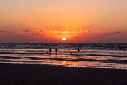 A group of people standing on a sandy beach near the shoreline, overlooking the ocean and enjoying the view