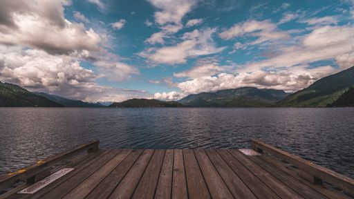 A mesmerizing view of a calm lake surrounded by mountains under a cloudy sky
