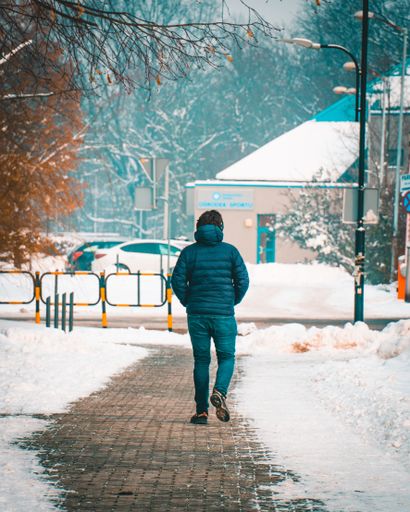A male in warm clothes walking through heavy snow in the park