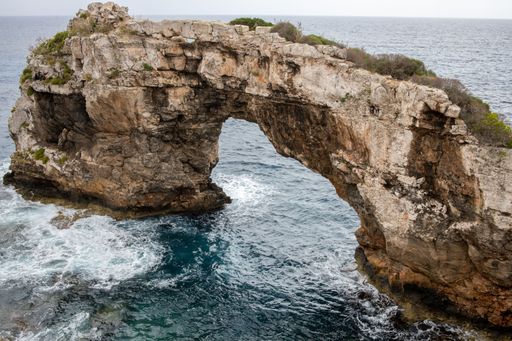 Aerial view of a majestic natural arch over the ocean, with towering cliffs jutting out of the crystal-clear waters