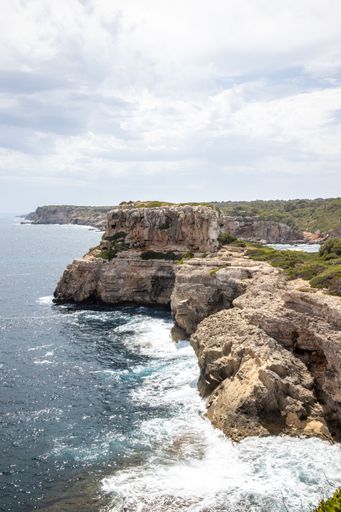 Two people are perched on the edge of a cliff overlooking a breathtaking view of a sparkling blue body of water