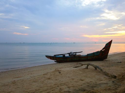 A wooden boat on a beach surrounded by the sea under a cloudy sky during the sunset