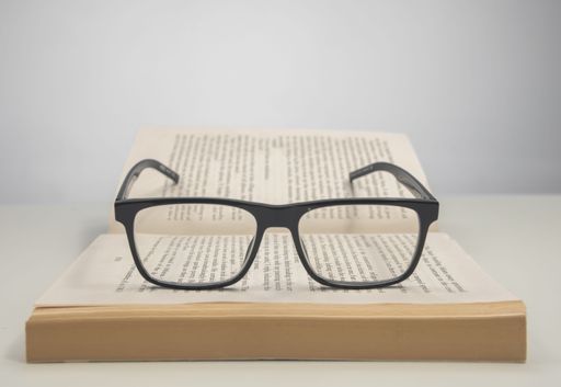 A closeup of reading glasses on an open book on a white surface