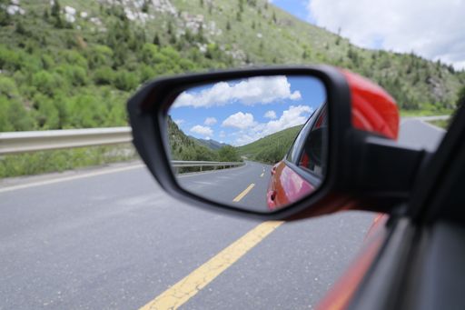 A closeup shot of a car's side mirror reflecting the road and green mountains.