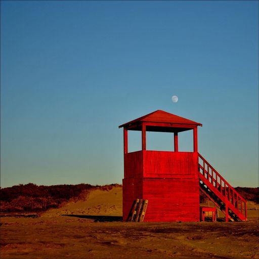 A red security guard booth located in Lido di Ostia, Lazio, Italy with the Moon in the background